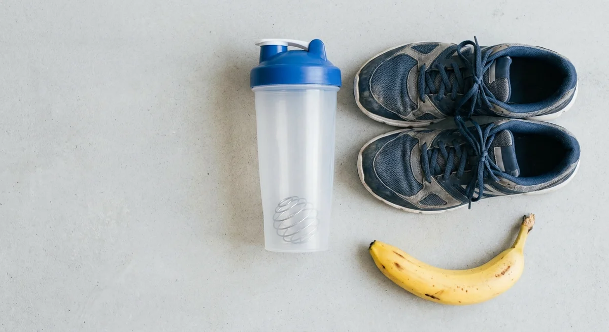 Protein shaker, running shoes, and banana laid out on a grey surface for post-cardio recovery