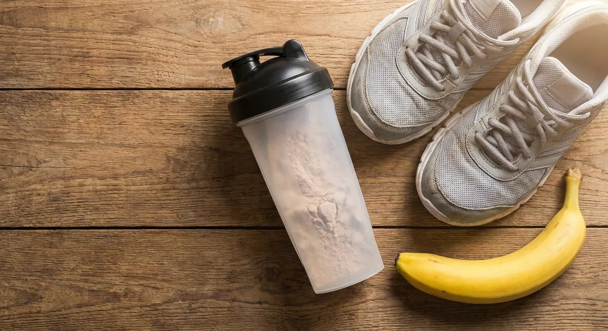 Protein shaker, running shoes, and banana laid out on a table for post-run recovery