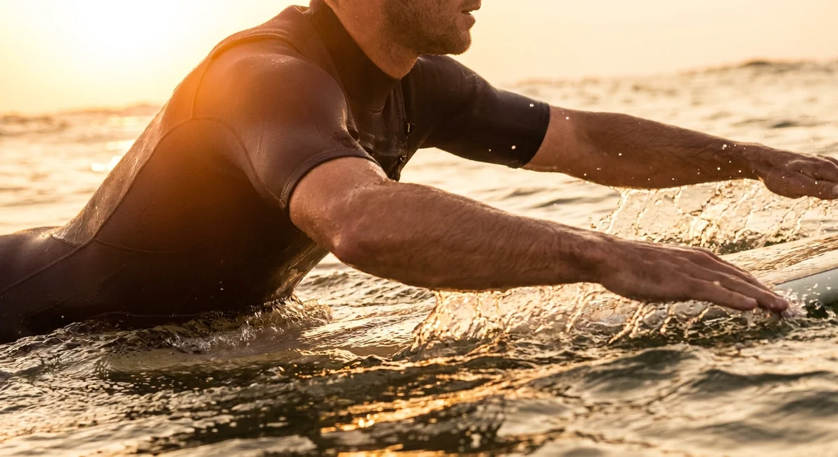 Surfer paddling through waves showing shoulder and back muscle engagement